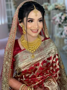 a woman in a red and gold bridal outfit with jewelry on her head, smiling at the camera