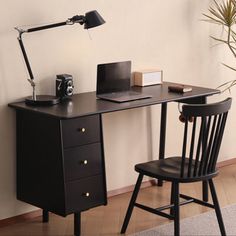 a desk with a laptop and a lamp on it next to a chair in front of a wall