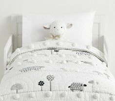 a white bed topped with a stuffed animal next to pillows and pillow cases on top of it