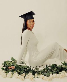 a woman wearing a graduation cap sitting on the ground with white roses and greenery