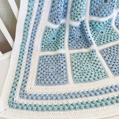 a crocheted blanket on top of a white bed next to a wooden chair