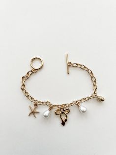 Gold charm bracelet. Charms include pearls, starfish, bow and acorn. Toggle Clasp. Gold Toggle Bracelet, How To Make A Charm Bracelet, Charm Bracelet Charms, Pearl Charm Bracelet, Bracelet Charms, Gold Charm Bracelet, Pearl Charms, Toggle Clasp, Gold Charm