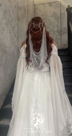 a woman in a white wedding dress walking down some stairs with her veil draped over her head