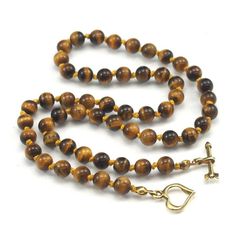 Tiger's Eye Necklace with Gold Plated Toggle Clasp Approx. 18 1/2" long Bead Size : 6mm Strung and knotted on silk cord Handcrafted at Beads of Paradise NYC Tiger’s Eye is a form of Chalcedony quartz, but is what is a known in mineralogy as a pseudomorph. The term comes from the Greek for "false form." Pseudomorphs form when one mineral replaces another. It began as the fibrous blue mineral called Crocidolite, which is made up of iron and sodium. The Crocidolite was gradually transformed into wh Adjustable Lariat Necklace With Gemstone Beads, Adjustable Single Strand Lariat Necklace With Round Beads, Gold Jewelry With Hand-knotted Round Beads, Adjustable Hand Knotted Necklaces, Gold Hand-knotted Necklace For Gift, Gold Hand Knotted Necklace For Gift, Handmade Toggle Necklace As Gift, Round Beads Single Strand Lariat Necklace As Gift, Handmade Adjustable Toggle Necklace As Gift