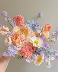 a bouquet of flowers is being held up by someone's hand in front of a wall