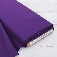 the purple fabric is folded on top of white wood planks and has a book in front of it