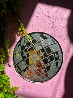 a round glass plate sitting on top of a pink wall next to a green plant