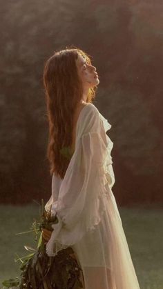 a woman with long hair wearing a white dress and holding a bouquet in her hand