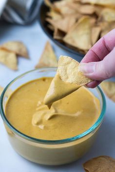 a hand dipping tortilla chips into a bowl of dip with tortilla chips on the side