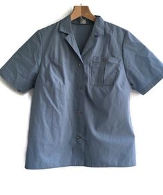 Vintage 80s blouse light blue short sleeve shirt size 38-40 Blue Collared Top With Pockets, Blue Top With Pockets And Collared Neckline, Collared Camp Shirt With Pockets For Work, Short Sleeve Camp Shirt With Pockets For Work, Solid Color Short Sleeve Tops With Pockets, Solid Short Sleeve Shirt With Camp Collar, Solid Short Sleeve Shirt With Buttons And Camp Collar, Fitted Short Sleeve Tops With Buttoned Pockets, Solid Short Sleeve Shirt With Camp Collar And Buttons