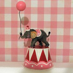 an elephant figurine holding a pink balloon on top of a circus tent table