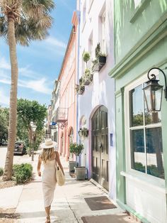 a woman walking down the sidewalk in front of a pink and green building with palm trees