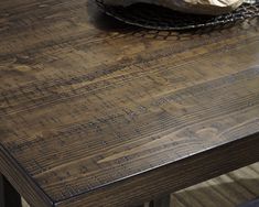 a close up of a wooden table with a basket on top of it and a bowl of fruit in the background