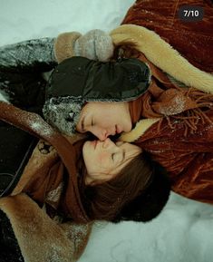 two women are laying in the snow with their heads touching each other's noses