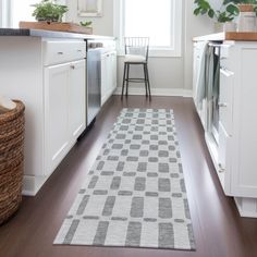 a kitchen with white cabinets and wooden flooring, along with a rug on the floor