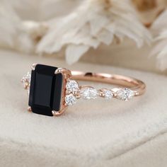 a black and white diamond ring sitting on top of a cushioned surface with flowers in the background