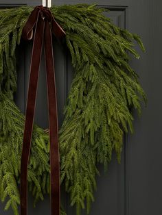 a christmas wreath hanging on a door with a brown ribbon around it and a bow