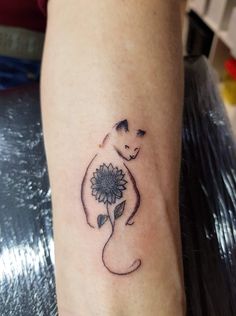 a cat with a sunflower tattoo on its leg is sitting next to a woman's arm