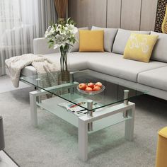 a glass coffee table with fruit on top in a living room area next to a couch