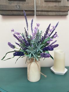 a vase filled with purple flowers sitting on top of a table next to a candle