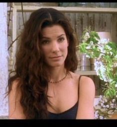 a woman with long hair sitting in front of a potted plant