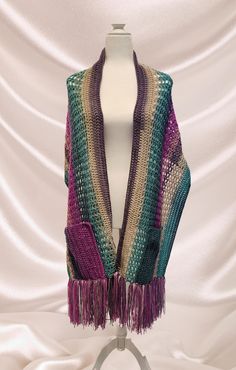 This hand knit pocket scarf is perfect when it's a little chilly, but you don't want to wear a coat. It is made in a beautiful multicolored pattern which includes shades of green, purple, pink, and cream. It will go perfectly with your favorite jeans, and the fringe at the bottom gives it a distinct boho flair! The yarn is composed of 30% wool and 70% acrylic. The wool content helps to keep you warm without adding a lot of weight. Purple Shawl For Fall, Multicolor Crochet Shawl For Fall, Bohemian Knitted Scarves For Fall, Purple Bohemian Shawl For Winter, Bohemian Yarn Scarves For Fall, Bohemian Knit Scarves For Fall, Multicolor Yarn Shawl For Fall, Bohemian Purple Shawl For Fall, Purple Bohemian Shawl For Fall