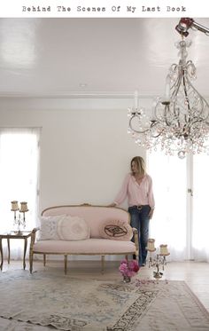 a woman standing next to a couch in a living room with chandelier above it