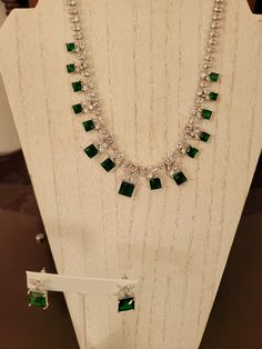 "The necklace has square cut emeralds that are one to six carats each for a total of 38 carats emerald.  The chain is done in 1mm round and square cut diamonds with 3mm diamond petal design above the emeralds.  It has 5 carats of diamond accents.    It is a non adjustable 16 inches with a fold over clasp closure.  The earrings are pierced and have a 5 carat square cut emerald stone with an \"x\" design .66 carat diamond accents.  Platinum plated." Formal White Gold Emerald Necklace With Jewels, Exquisite Emerald Diamond Necklace, Dazzling Jeweled Emerald Necklace For Formal Events, Exquisite Emerald Necklace For Formal Occasions, Luxury Emerald Jewelry For Formal Occasions, Elegant Emerald Necklace For Formal Occasion, Hand Set Emerald Necklaces For Formal Occasions, Emerald Diamond Necklace For Formal Occasions, Formal Emerald Diamond Necklace In White Gold