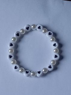 a white bracelet with black hearts and silver beads on top of a blue sheet of paper