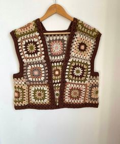 a crocheted vest hanging on a wall with a wooden hanger in front of it