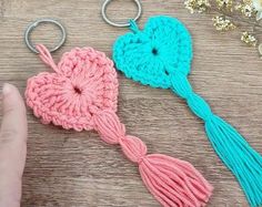 two crocheted heart shaped key chains with tassels on the ends, one being held by a hand