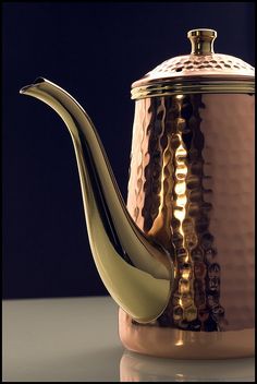 a copper tea pot with a metal lid on a white countertop next to a black background