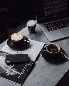 a cup of coffee sitting on top of a table next to a book and laptop