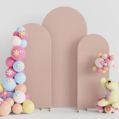 a teddy bear sitting in front of balloons on the floor next to a pink wall