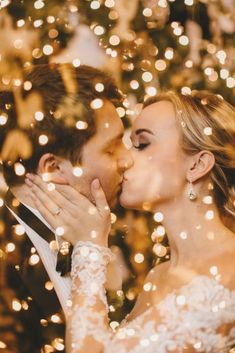 a bride and groom kissing in front of a christmas tree with lights all around them