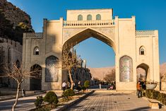 people are standing in front of an ornate arch on a sunny day with mountains in the background