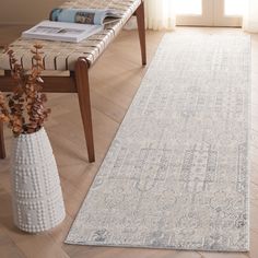 a large white rug on the floor next to a chair and table with flowers in it