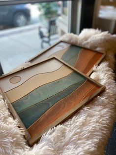 two wooden trays sitting on top of a fluffy white blanket next to a window