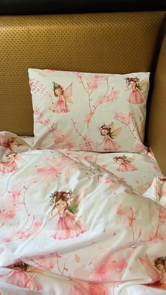 an unmade bed with pink flowers and fairy dolls on the comforter, along with two pillows