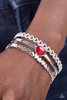 Three bands of silver arc across the wrist to create a romantic-inspired cuff. A row of white rhinestone-studded hearts are turned on their sides, gracing the top band of the cuff while solid silver hearts alternate end-over-end to create the bottom band. A sleek bar of silver topped with a red, heart-shaped, cat's eye stone falls between the outer bands, emerging as a polished focal point in a whimsical finish.

 Sold as one individual bracelet. Sleek Bar, Mobile Boutique, Win My Heart, Cats Eye Stone, Top Band, Silver Tops, Paparazzi Accessories, White Rhinestone, Eye Stone