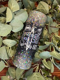 a glittered water bottle sitting on top of some green leaves and plants next to it