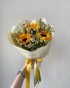 a person holding a bouquet of sunflowers with yellow ribbons around it's ends