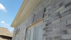 an old brick building with white curtains on the window sill and blue sky in the background