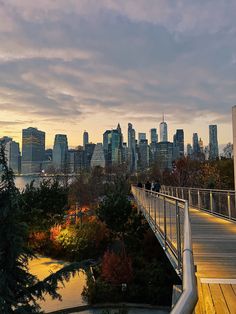 the city skyline is lit up at dusk as people walk across a bridge over water