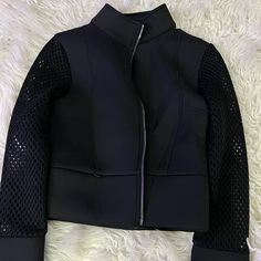 a black jacket with mesh sleeves and zippers on the front, sitting on a white furnishing