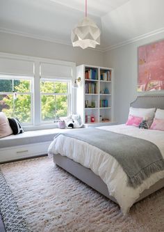 a bedroom with a bed, window seat and bookshelf in the corner next to it