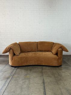 a brown couch sitting on top of a cement floor next to a white brick wall