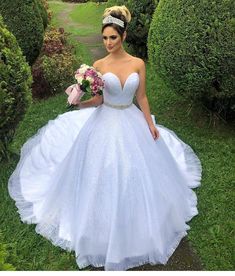 a woman in a white ball gown standing on the grass with her bouquet and flowers