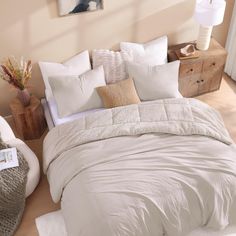 a bed with white comforters and pillows in a room next to a dresser on the floor