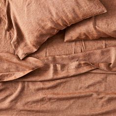 an unmade bed with brown sheets and pillows